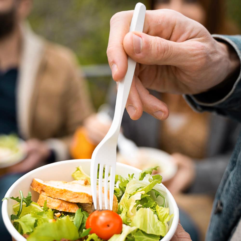 Forchetta compostabile in bioplastica utilizzata per gustare un’insalata con pollo e pomodoro, in un contesto conviviale e sostenibile all’aperto.
