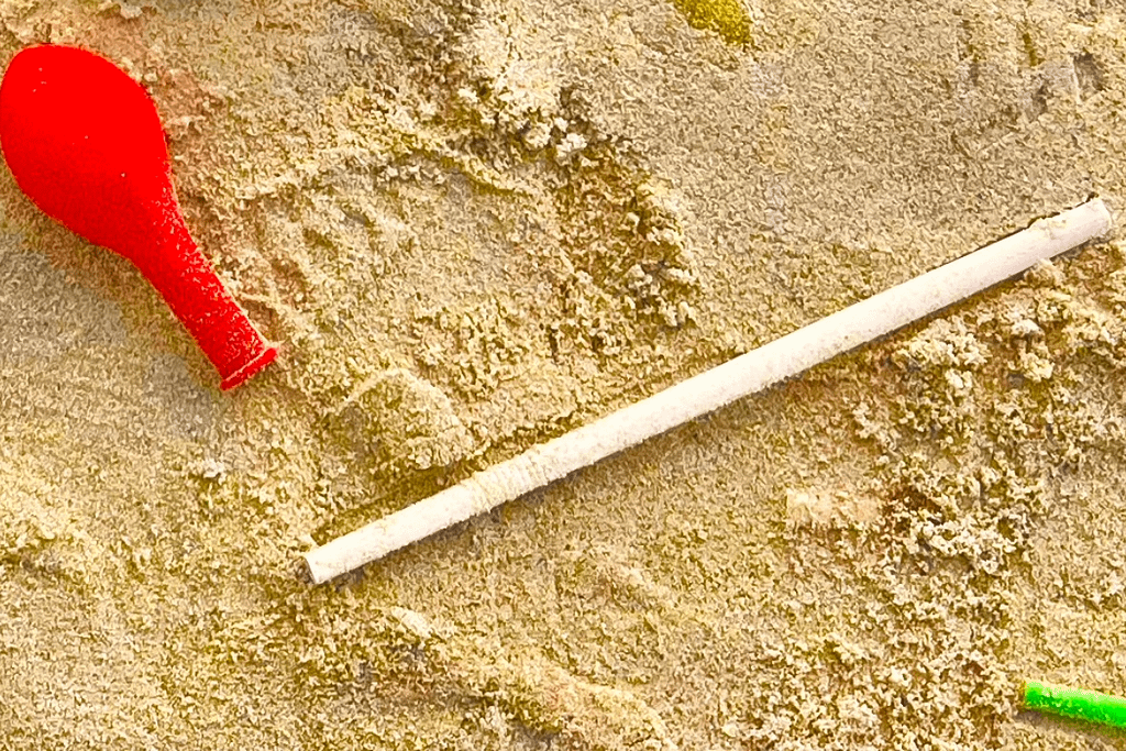 Cannuccia di plastica bianca e frammento di palloncino rosso sulla sabbia.