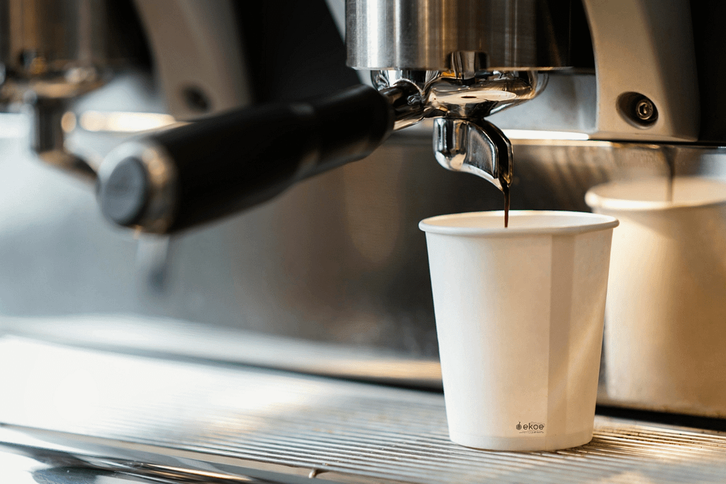 Caffè espresso versato in un bicchiere compostabile sotto una macchina da caffè professionale.