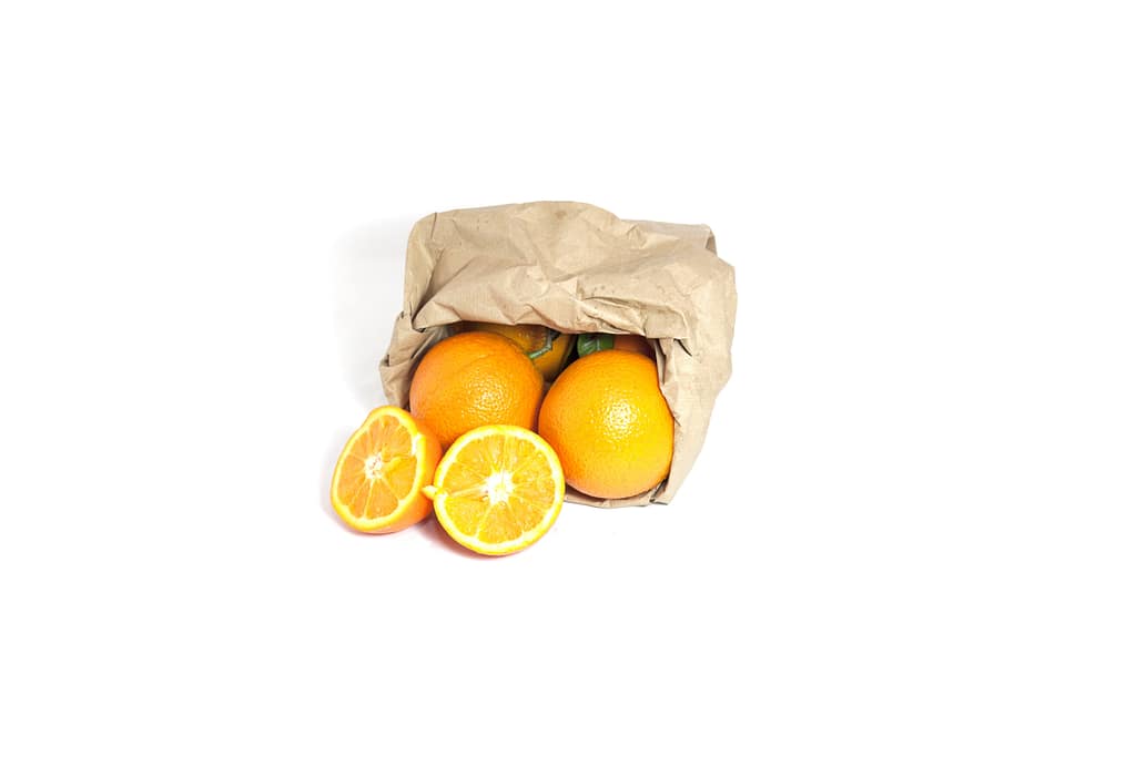 Sacchetto in carta per ortofrutta con arance fresche su sfondo chiaro.