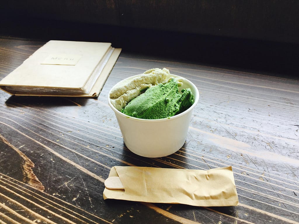 Coppetta compostabile con gelato e paletta in legno imbustata su tavolo in legno scuro